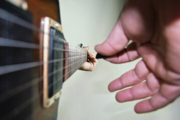 Pessoa a tocar uma guitarra eletroacustica - pormenor da mão direita com palheta e mão esquerda focada num acorde - braço da guitarra em linha de fuga - guitarra electrica de caixa oca - jazz, blues