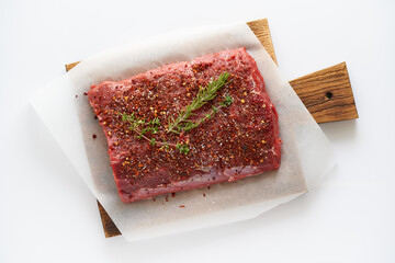 Big whole piece of raw beef meat, striploin on white parchment paper on craft background, zero waste packing. Steak with seasoning and salt. Top view, close up