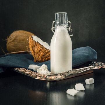 Bottle of coconat milk  and coconuts  on a blue cloth.  Healthy dairy-free alternative milk on a black background.   Powdered coconut milk on a teaspoon. Superfoods .Non-allergy ingredients for coffee