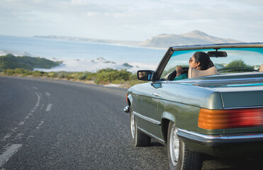 Mixed race woman driving on sunny day in convertible car holding driving wheel
