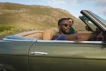 Diverse couple driving on sunny day in convertible car and smiling