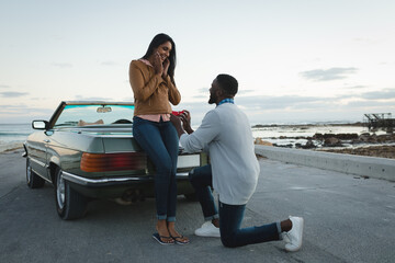 Diverse couple standing by convertible car man is proposing to woman