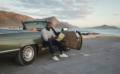 African american man sitting in convertible car and looking at map