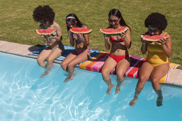 Diverse group of female friends eating watermelon sitting at the poolside