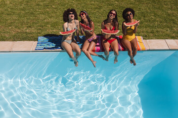 Diverse group of female friends eating watermelon sitting at the poolside talking