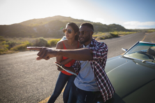 Diverse couple on sunny day standing by convertible car looking at a map - Powered by Adobe
