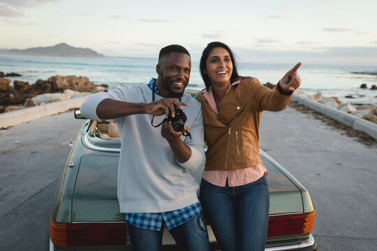 Diverse couple standing by a convertible car and taking photos with camera