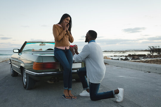 Diverse couple standing by convertible car man is proposing to woman
