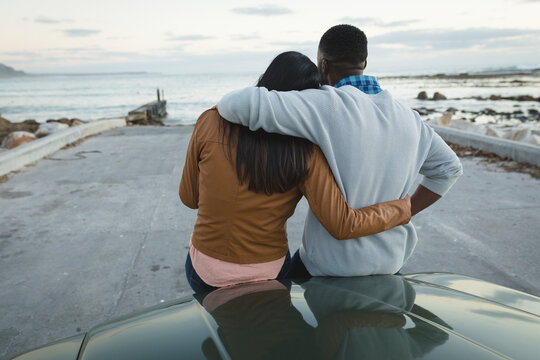 Diverse couple sitting on a convertible car and embracing