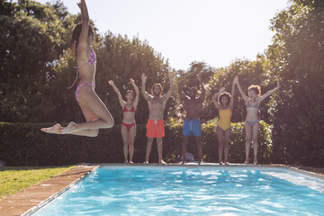 Diverse group of friends having fun and jumping into water at a pool party