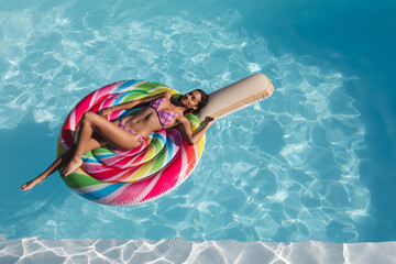 Mixed race woman sunbathing on inflatable in swimming pool