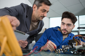 mentor guiding apprentice engineer when using a multimeter