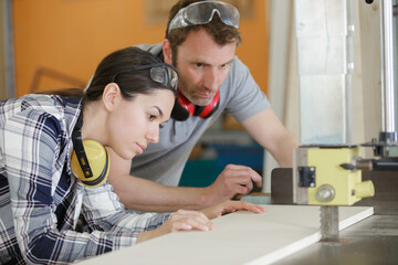 carpenter training female apprentice to use mechanized saw