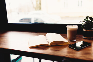 Cup of coffee, notebook, phone at table in cafe. Blurred background