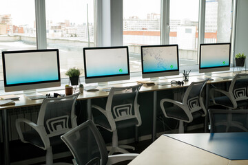 Row of computer monitors standing on desks against large windows in call center