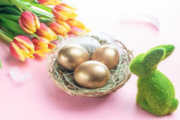 Egg color. Happy Easter decoration: golden colour eggs in basket with spring tulips, white feathers on pastel pink background. Foil minimalist egg design, modern template.