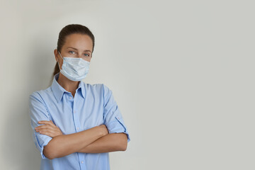 Young woman in blue shirt with arms crossed looking at the camera, wearing protective face mask, correct wearing masks should cover nose as well