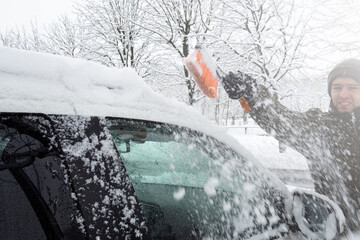 Removing snow from car with a brush. Man cleans his car after a snowstorm.