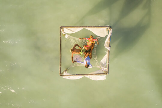 Aerial view of three people relaxing on a hammock along the beach of Villa Isabela, Puerto Plata, Dominican Republic. - Powered by Adobe