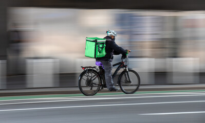 Delivery man with green bag on back while riding a bike