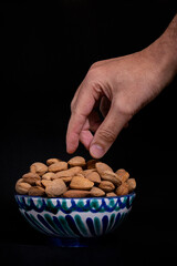 hand picking almonds in a ceramic bowl on a black background