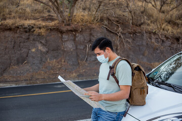 Viajero masculino con una mochila y mapas con una máscara sanitaria de pie en la carretera