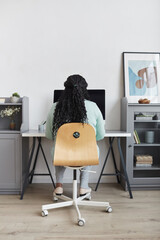 Minimal back view at curvy African American woman using PC at home workplace in modern interior, copy space