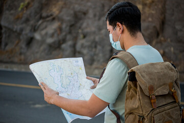 Viajero masculino con una mochila y mapas con una máscara sanitaria de pie en la carretera