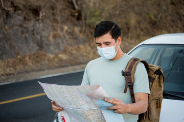 Viajero masculino con una mochila y mapas con una máscara sanitaria de pie en la carretera