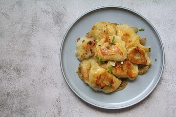fried dumplings, crispy dumplings with fried onion, round plate full of hot dumplings sprinkled with green onions
