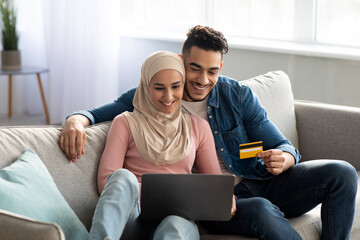 Positive middle-eastern couple buying plane tickets online, using laptop