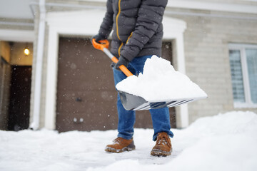 A mature man clean path near house from snow during strong blizzard. Person shoveling snow out of...