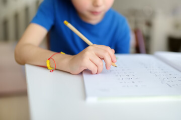 Elementary student boy doing homework at home. Child learning to count, solves arithmetic examples, doing exercises in workbook. Math tutorial. Preparing preschooler baby for school. Education - obrazy, fototapety, plakaty