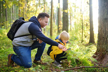 School boy and his father hiking together and exploring nature with magnifying glass. Child with his dad spend quality family time together in the sunny summer forest.