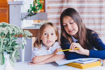 Two girls in school uniforms are sitting at a desk solving problems, examples, writing dictation,...