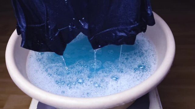 woman washes with her hands blue men's panties in a basin, knitted underwear, clean clothes concept, scandal in the Russian Federal Security Service