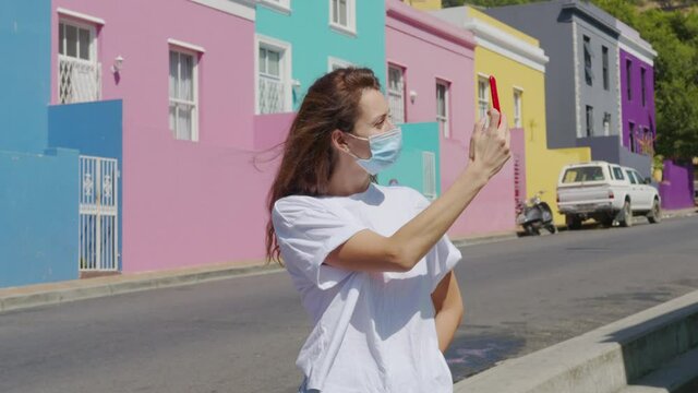 Woman tourist in pandemic shoots on the phone in Cape town Bo-Kaap Malay area, perspective of cobble stone street, colored terrace houses, South Africa.