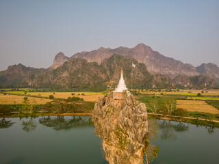 Aerial view of Kyaut Ka Latt Pagoda on a small island in the middle of a small lake with a mountain range in background, Hpa-an Township, Myanmar.