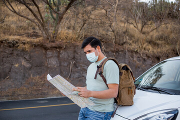 Viajero masculino con una mochila y mapas con una máscara sanitaria de pie en la carretera