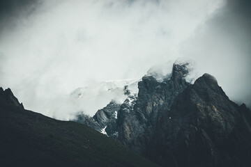 Dark atmospheric surreal landscape with dark rocky mountain top in low clouds in gray cloudy sky....