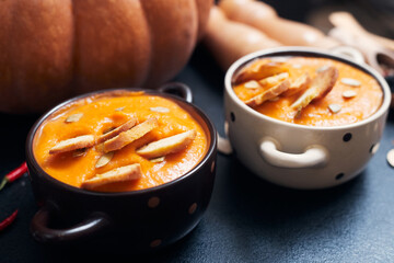 pumpkin cream soup with croutons on a black table with spices