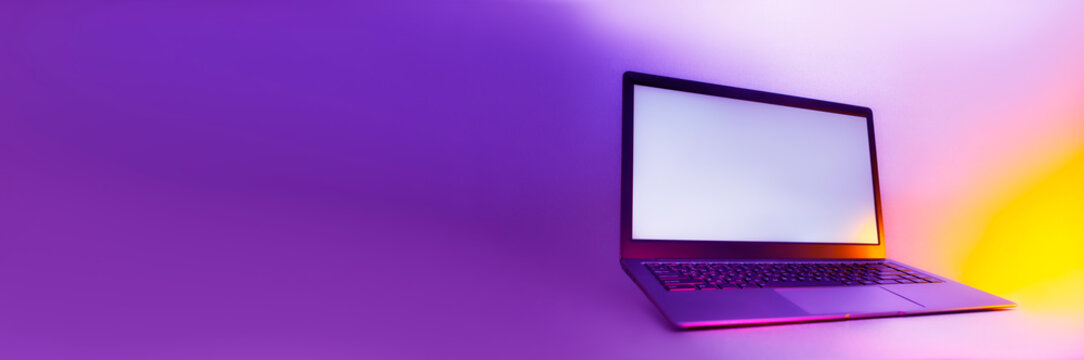 Slim Modern Laptop With White Screen On The Background Creative Light. Mockup In Colorful Bright Neon UV Blue And Purple Lights.