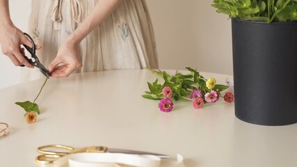 Mujer cortando el pedúnculo de una flor fucsia. Flores sobre la mesa