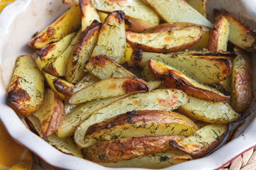 Rustic potatoes in a ceramic bowl with a yellow towel. Potatoes in oil with dill and garlic.