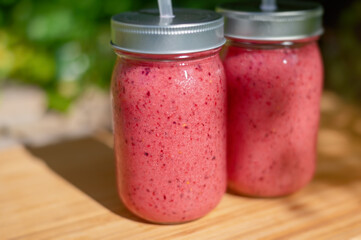 Smoothies in a glass jar with a straw. Orange, red berries and banana smoothie.
