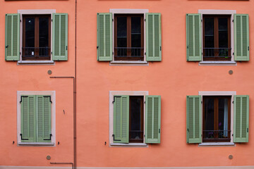 Fototapeta na wymiar Pink building faced with six green windows, one of which is closed, Italy, Alps