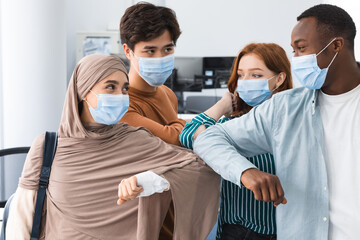 Diverse people wearing face masks greeting and bumping elbows