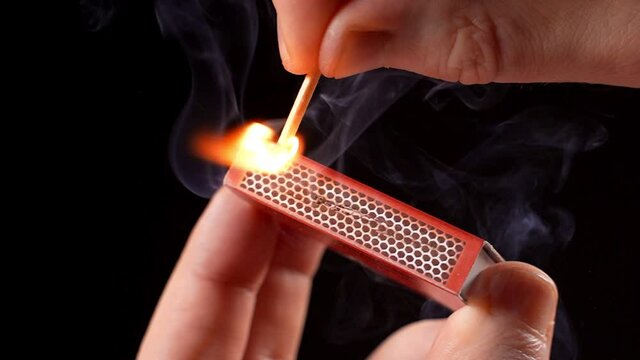 Man lights a match on black background in slow motion.