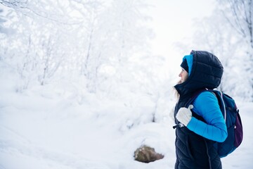 A blonde tourist dressed in warm clothes with a backpack on a mountain trail in winter on a frosty day in the mountains.
