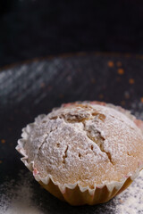 cupcake in powdered sugar on a plate on a black background